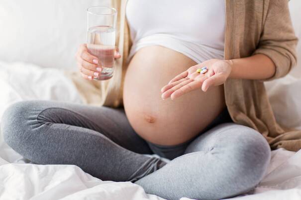Gravid kvinde med et glas vand og vitaminpiller.